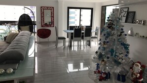 A modern living room with a sofa, a dining table, and chairs. A white Christmas tree with ornaments and a Santa figure is in the corner. - COMPLETE LEISURE COVERAGE  (Praia Grande)