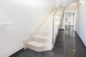 A modern staircase with glass railings, leading to a dining area with white chairs and a table.