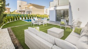 Eine moderne Terrassenanlage mit Pool, weißen Korbmöbeln und einem gepflegten Rasen.