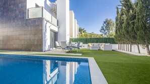 Ein moderner Poolbereich im Freien mit einem klaren, blauen Pool, einem gepflegten Rasen und einer Sitzgelegenheit mit Gartenmöbeln.