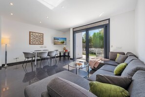 A modern living room with a glass coffee table, grey sofas, and a dining area with chairs. - House with pool a few steps from the beach (Alcúdia)