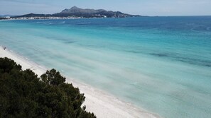 Ein Strand mit klarem türkisblauem Wasser, einem sandigen Ufer und einem gebirgigen Hintergrund.