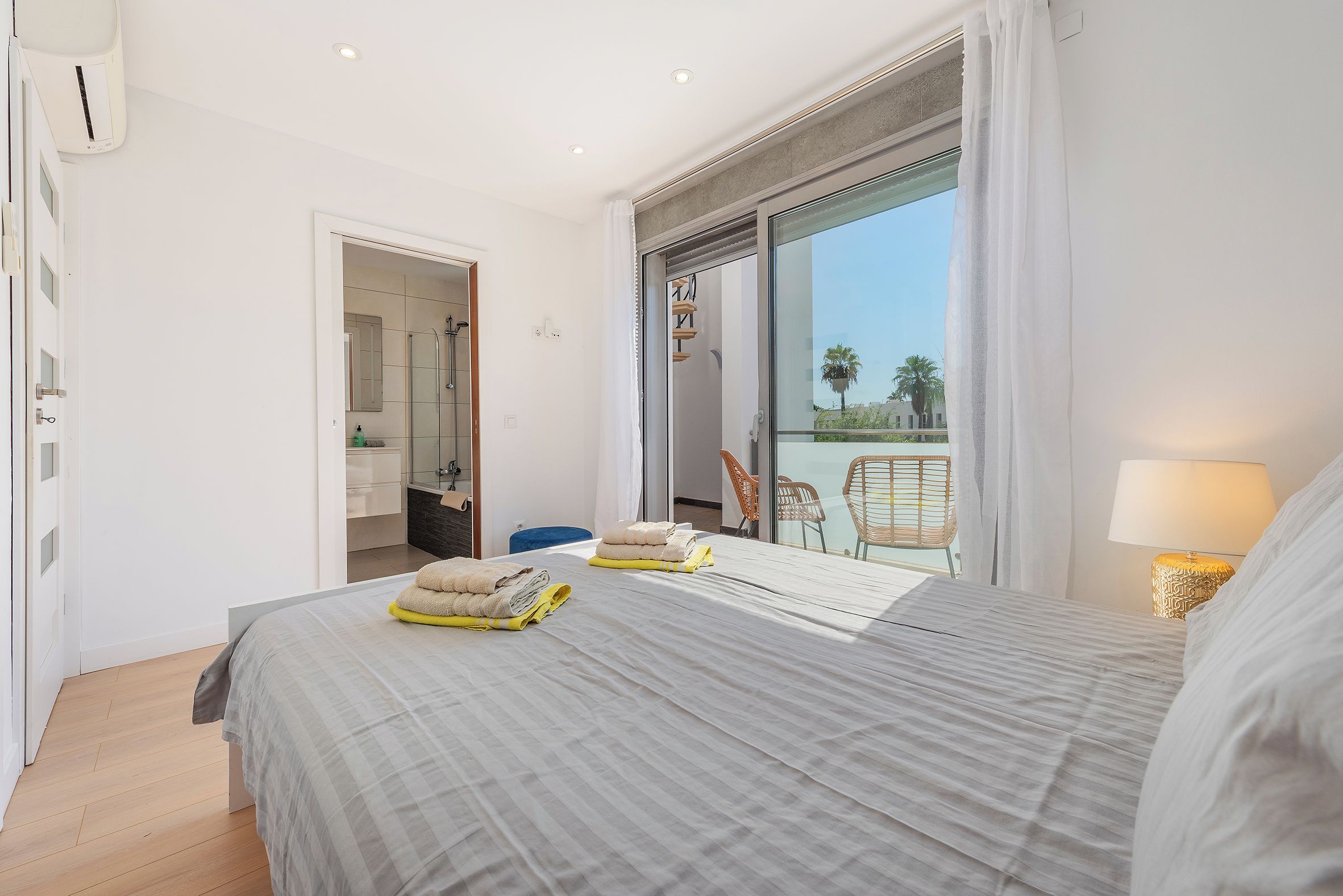 A hotel room with a bed, a bathroom, and a balcony with chairs.