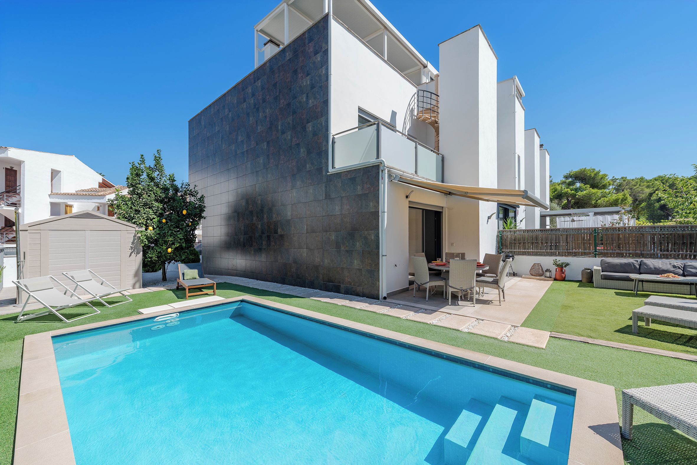 A modern two-story house with a swimming pool, outdoor furniture, and a well-maintained garden.