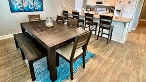 Un coin repas avec une table et des chaises en bois foncé, un tapis bleu et un mur orné d’œuvres d’art abstraites.