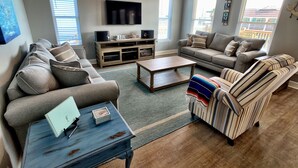 Un salon avec un canapé gris, un fauteuil à rayures, une table basse et un téléviseur fixé au mur.