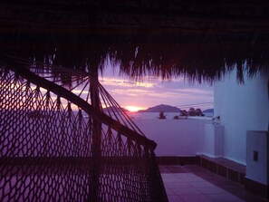 A balcony with a view of the sunset over water, a thatched roof, and a tiled floor. - Colonial Home with ocean views close to the beach in Mazatlan (Mazatlán)