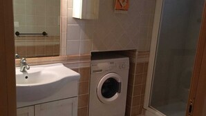 A compact bathroom with a sink, washing machine, toilet, and a shower area. - Apartment on a family house (Roma)