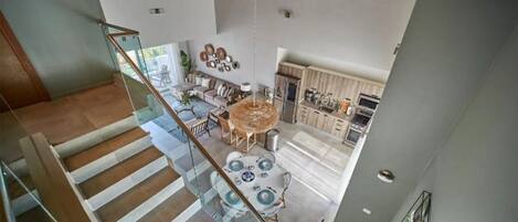Un intérieur spacieux avec un plafond haut, un coin repas doté d’une table ronde et une cuisine avec des meubles en bois.