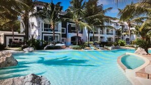 A resort with a large pool surrounded by palm trees and a multi-story building with balconies. - New loft duplex with rooftop deck (Dominicus)