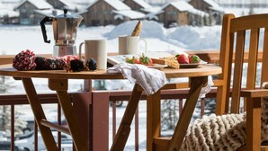 A wooden deck with a table set for breakfast, overlooking a snowy landscape with houses in the background. - Outpost: Crystal Springs 405 - Ski-In/Ski-Out! (Teton Village)