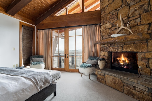 Une chambre avec une cheminée en pierre, une grande fenêtre et un balcon.