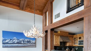 A spacious dining area with a long wooden table and modern chairs, a kitchen with wooden cabinets and stainless steel appliances, and a large framed picture of a snowy mountain landscape on the wall. - Outpost: Crystal Springs 405 - Ski-In/Ski-Out! (Teton Village)