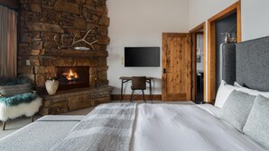 A bedroom with a stone fireplace, a bed, a desk, and a television. - Outpost: Crystal Springs 405 - Ski-In/Ski-Out! (Teton Village)