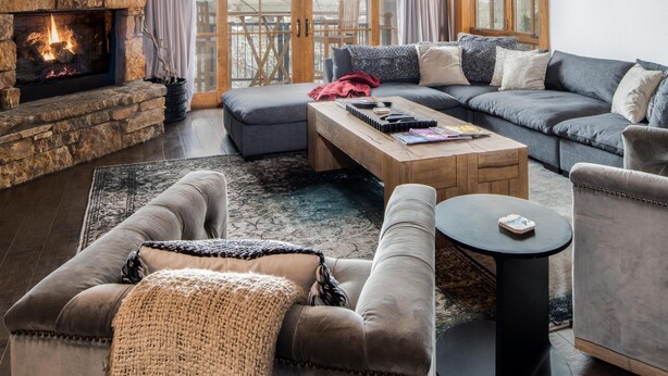 A cozy living room with a stone fireplace, wooden ceiling beams, and a large window offering a view of the outdoors. - Outpost: Crystal Springs 405 - Ski-In/Ski-Out! (Teton Village)