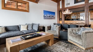 A spacious living area with a wooden ceiling, a large window, a dining table, and a kitchen in the background. - Outpost: Crystal Springs 405 - Ski-In/Ski-Out! (Teton Village)