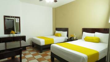A hotel room with two beds, a desk, a chair, a ceiling fan, and a mirror.
