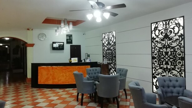 Un área de recepción con mostrador de registro, varias sillas, un ventilador de techo y paneles decorativos.