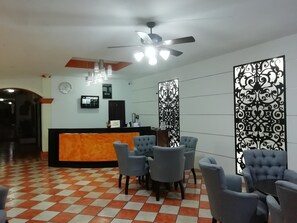 A reception area with a check-in counter, several chairs, a ceiling fan, and decorative panels. - Hotel Los Girasoles (Tepic)