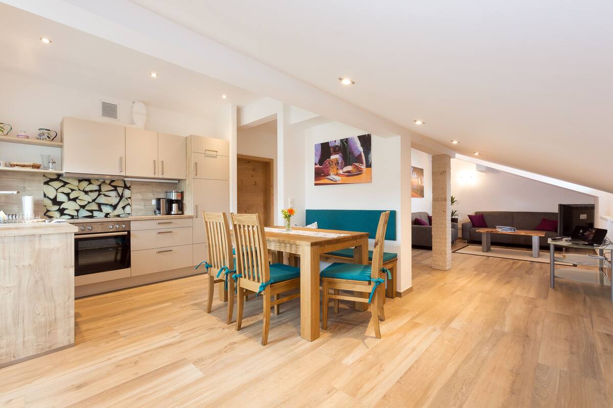 A modern kitchen with wooden cabinets, a dining area with a table and chairs, and a living room with a sofa and a coffee table.