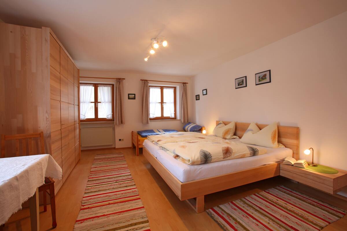 A bedroom with a bed, bedside table, nightstand, and a window with curtains.
