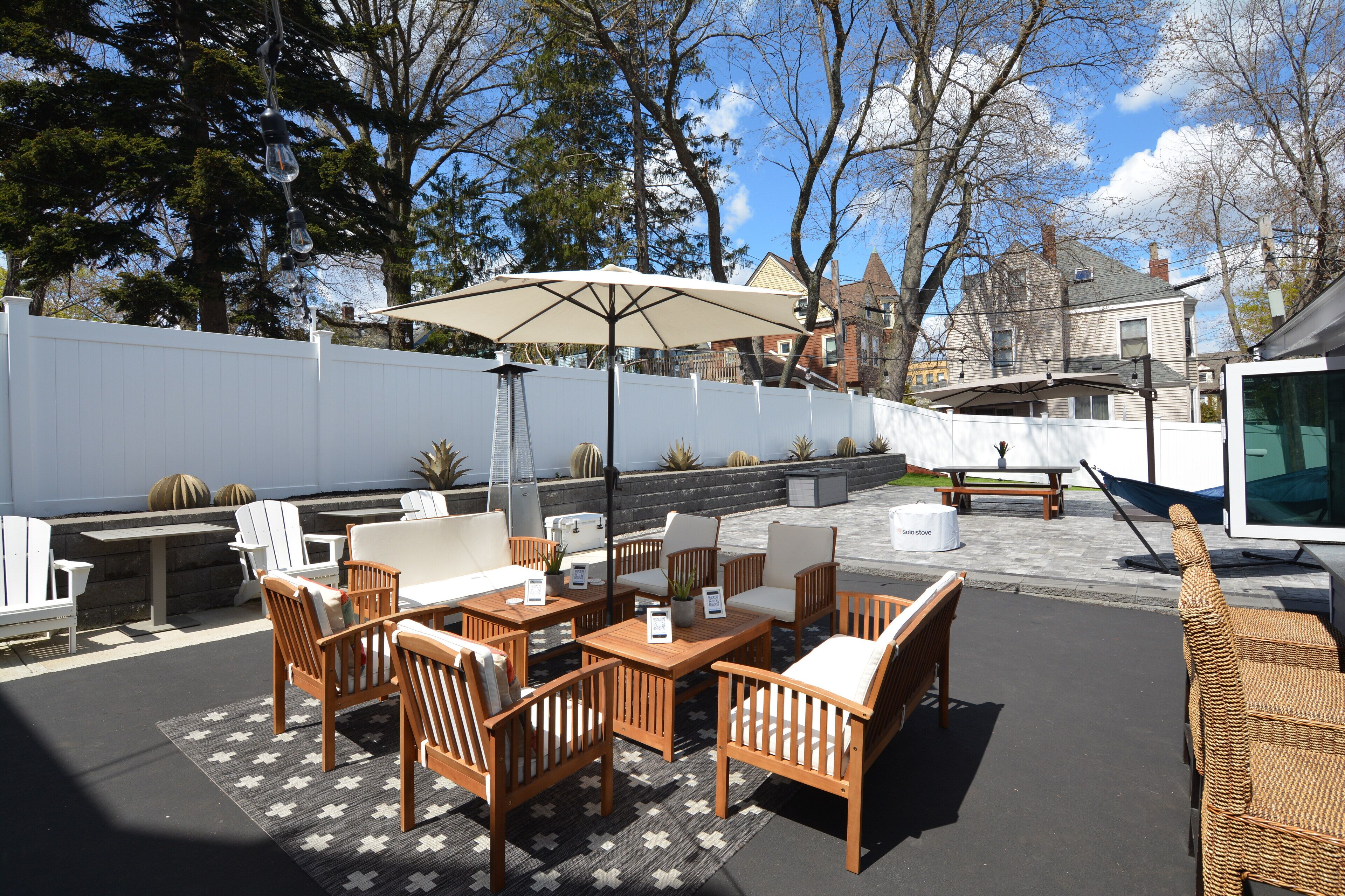 An outdoor patio with wooden furniture, a large umbrella, and a view of the neighborhood.