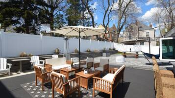 An outdoor patio with wooden furniture, a large umbrella, and a view of the neighborhood.