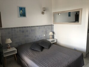 A bedroom with a bed, two bedside lamps, a wall-mounted mirror, and a framed picture.