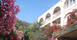 Un bâtiment doté de nombreux balcons et d’arcades, entouré d’une végétation luxuriante et de plantes en fleurs.