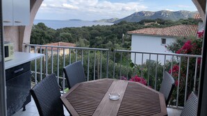 Een balkon met een tafel en stoelen, met uitzicht op een prachtig zee- en berglandschap.