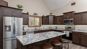 A modern kitchen with dark wood cabinets, stainless steel appliances, a large marble island, and a window with a view of trees. - Summit View Cabin Rental (British Columbia)