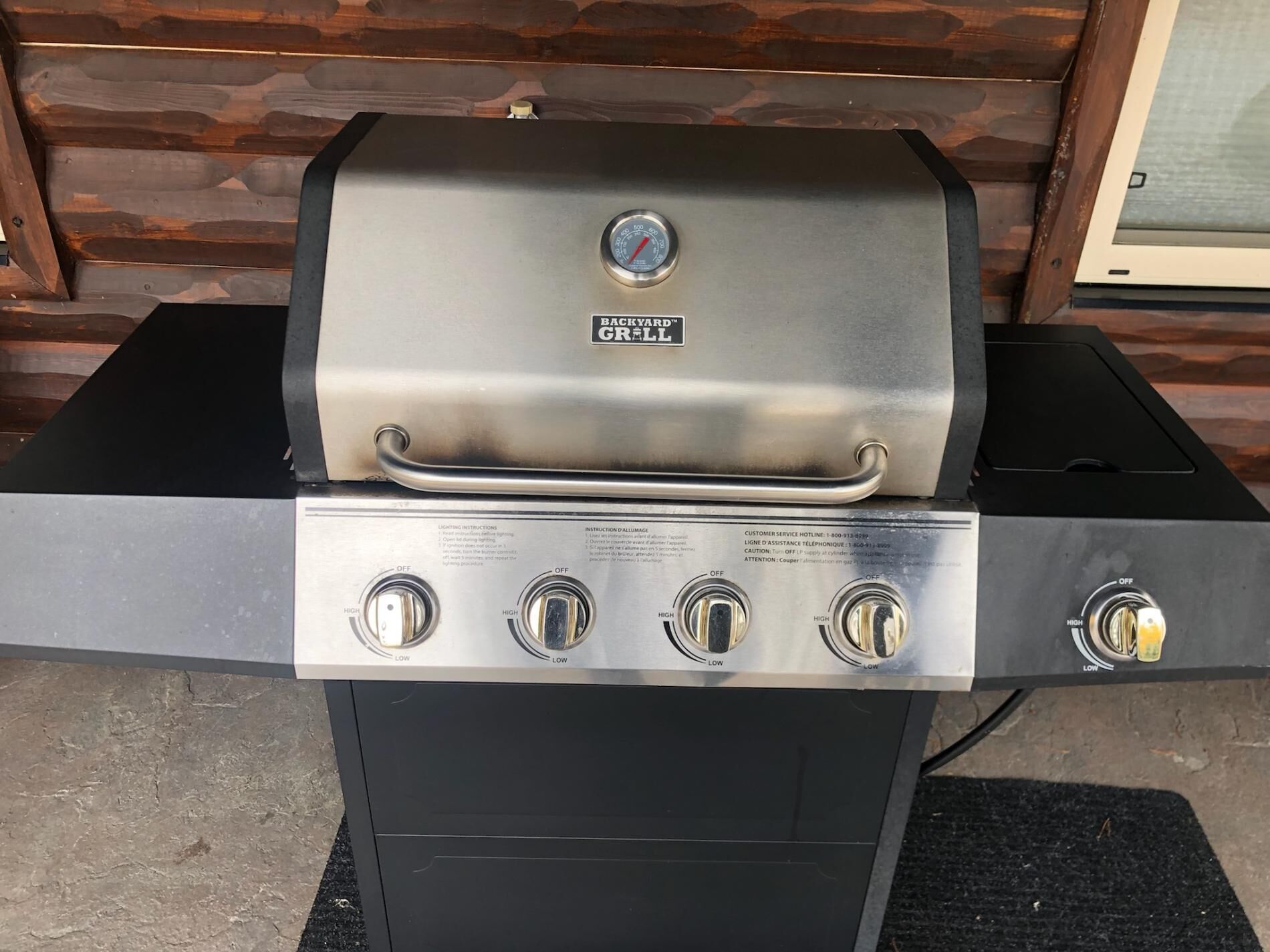 A stainless steel Backyard Grill with four burners and a thermometer gauge.