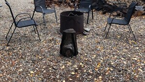 A gravel area with four black metal chairs arranged around a central fire pit. - Summit View Cabin Rental (British Columbia)