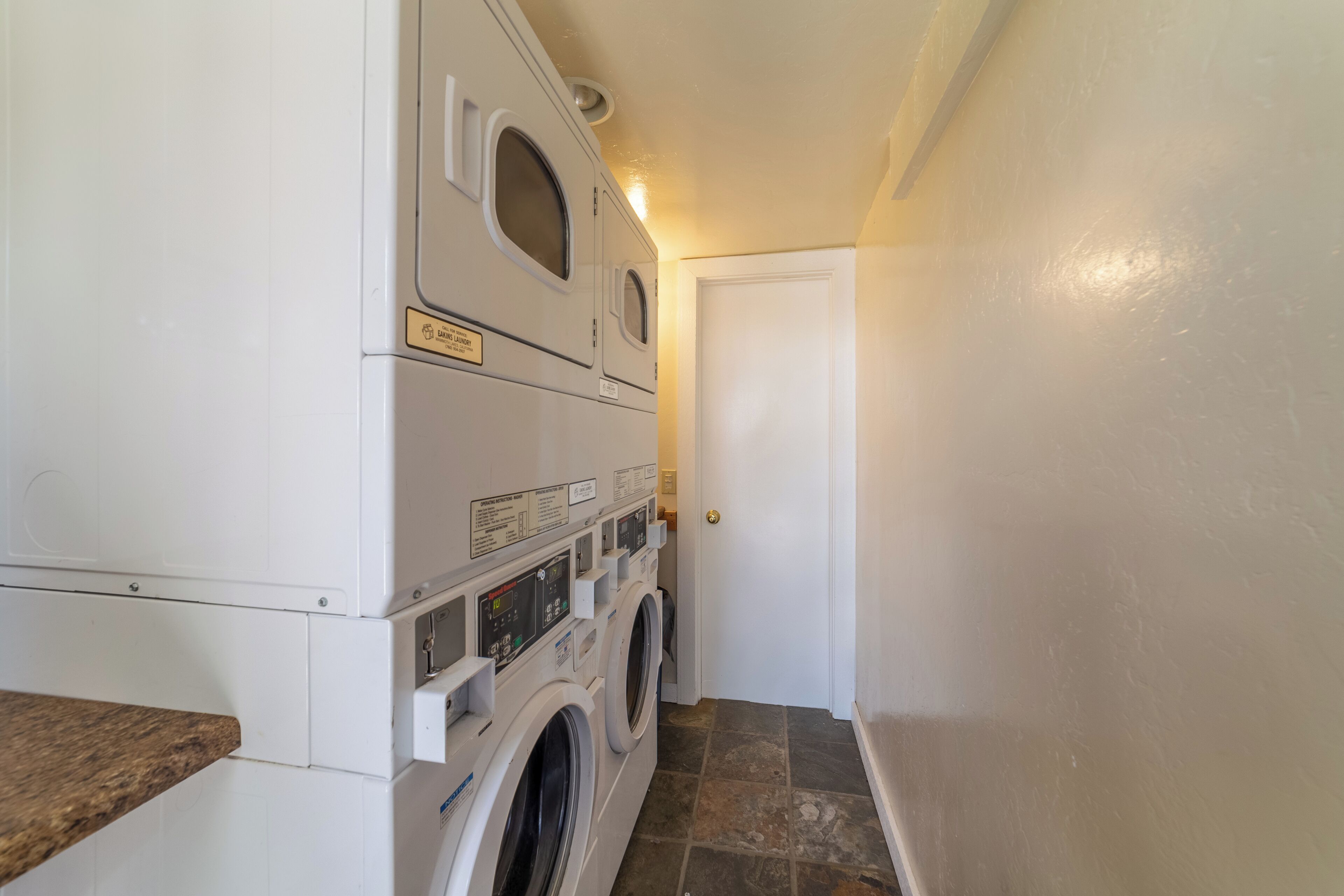 Une buanderie équipée de machines à laver et de sèche-linge superposés, d’un plan de travail et d’une porte.