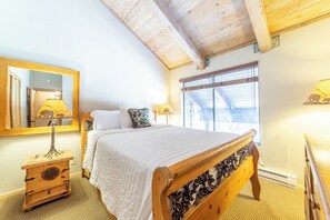 A bedroom with a wooden bed, a nightstand, a mirror, and a window with blinds. - Ski-Back Condo Near Village & Gondola 420 (Mammoth Lakes)