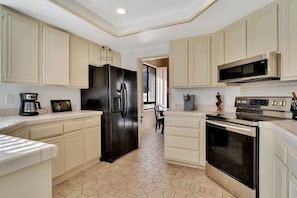 A kitchen with white cabinetry, a black refrigerator, a microwave, an oven, and a coffee maker. - Golfer's Paradise | 3BR Santa Rosa Cove (La Quinta)