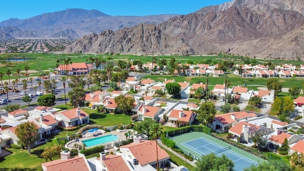 A residential area with houses, a swimming pool, tennis courts, and mountains in the background. - Golfer's Paradise | 3BR Santa Rosa Cove (La Quinta)