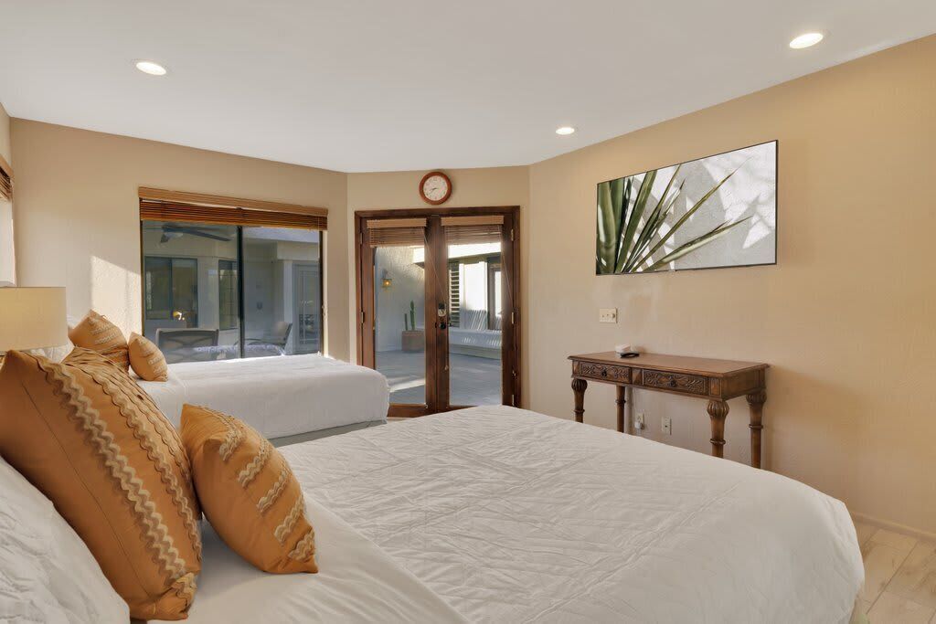 A hotel room with two beds, a wooden nightstand, a wall clock, and a large window.
