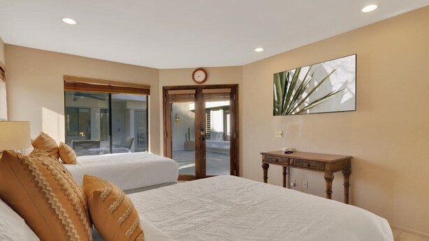 A hotel room with two beds, a wooden nightstand, a wall clock, and a large window. - Golfer's Paradise | 3BR Santa Rosa Cove (La Quinta)