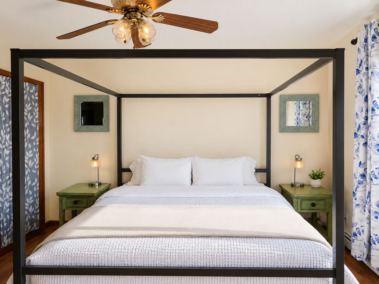 Un lit à baldaquin avec un ventilateur de plafond, deux tables de chevet avec des lampes et des miroirs fixés au mur.