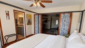 Une chambre avec un grand lit, un ventilateur de plafond et une vue sur la cuisine.