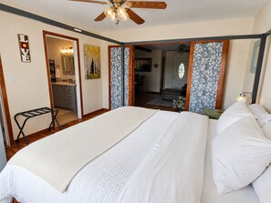 Un dormitorio con una cama grande, un ventilador de techo y vista a la cocina.