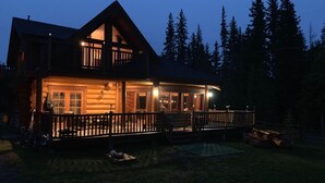 Eine zweistöckige Blockhütte mit Balkon und einer Terrasse, umgeben von Bäumen.