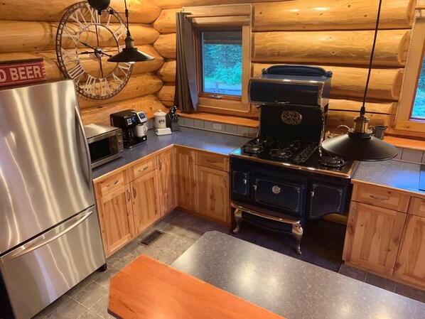 A log cabin kitchen with a stainless steel refrigerator, a coffee maker, a microwave, a stove, wooden cabinets, and a clock. - Custom built log home surrounded by lakes (Logan Lake)