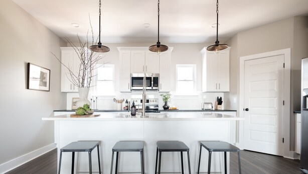 Una cocina moderna con armarios blancos, una isla central con taburetes de bar, electrodomésticos de acero inoxidable e iluminación colgante.