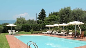 A swimming pool with tiled edges, surrounded by lounge chairs and umbrellas, set against a backdrop of trees and a clear sky. - Lovely apartment in villa for 6 people with WIFI, pool, TV, patio and pets allowed (Pescia)