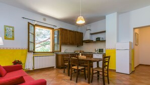 A compact kitchen with wooden cabinets, a dining table with chairs, a red sofa, and a window with a view of trees. - Lovely apartment in villa for 4 people with WIFI, pool, TV, patio, pets allowed and panoramic view (Montespertoli)