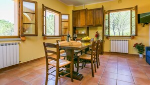 Une cuisine avec des meubles en bois, une table à manger avec des chaises et un téléviseur fixé au mur.