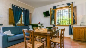 A cozy living room with a sofa, a dining table with chairs, a TV mounted on the wall, and a window with curtains. - Lovely apartment in villa for 4 people with pool, WIFI, TV, patio, pets allowed and panoramic view (Montespertoli)