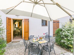 A patio with a round table and chairs, an umbrella, and a wooden door leading to a room.